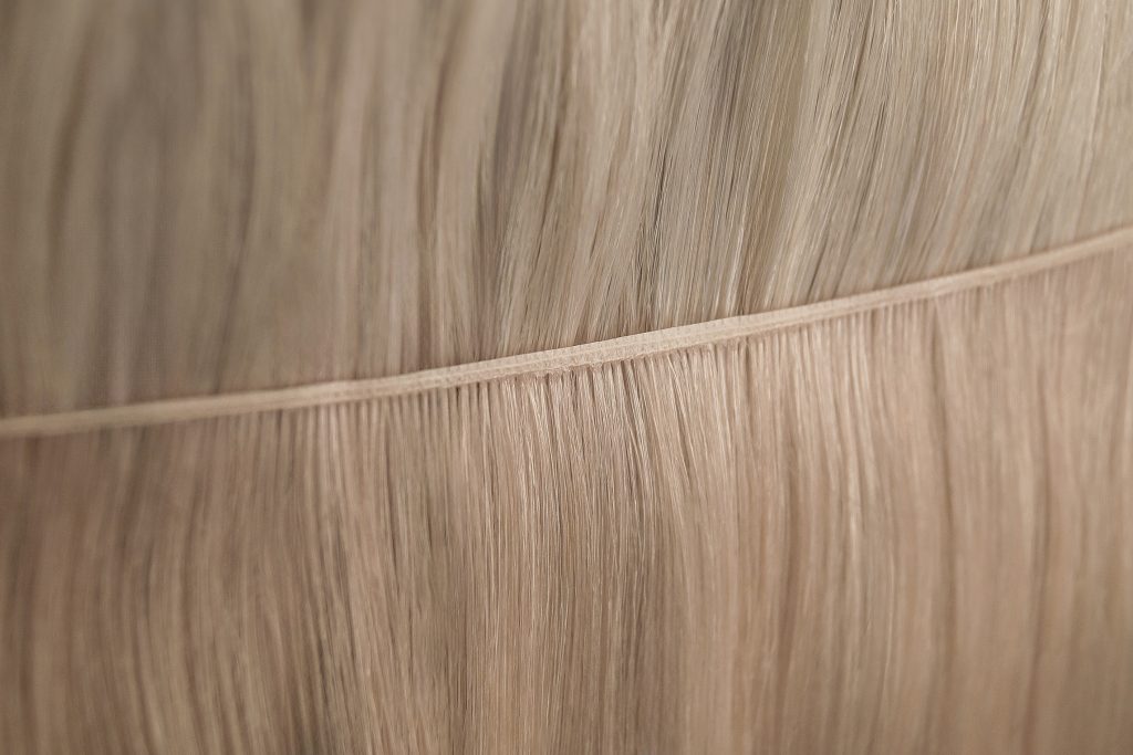Nahaufnahme einer hochwertigen, blonden Premium‑Tresse zur Haarverlängerung: fein vernähte Kante, seidig fallende Strähnen mit natürlichem Glanz